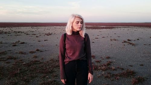 Thoughtful woman standing at beach against sky