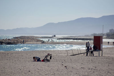 People at beach against clear sky during sunny day