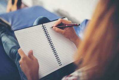 Woman writing on book while relaxing on sofa at home