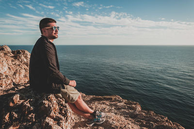 Man sitting on rock by sea against sky