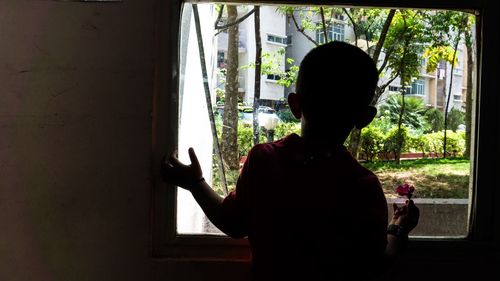 Rear view of silhouette woman standing against window at home