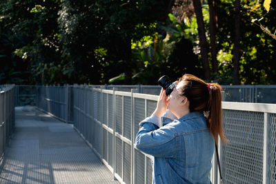 Side view of mid adult woman photographing on footbridge