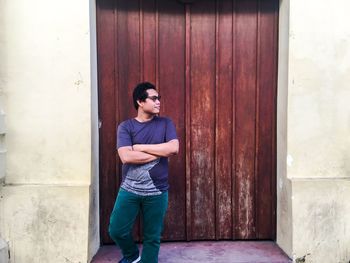 Young man with arms crossed standing against wooden door