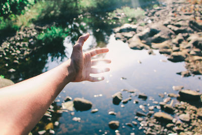 Cropped hand reaching towards lake on sunny day