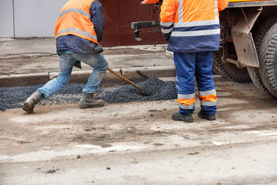 A road maintenance worker distributes fresh asphalt with a shovel at the patching of the road.