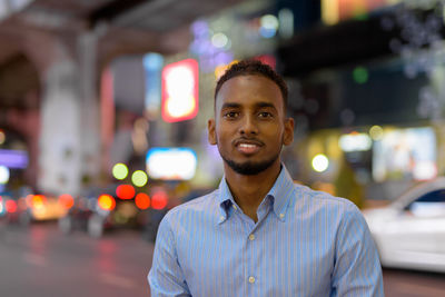 Portrait of young man standing against illuminated city at night