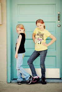 Full length portrait of sisters standing against closed door