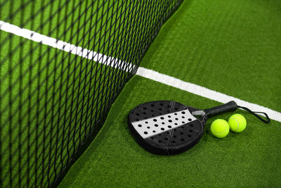 Closeup view of a paddle racket and balls in a padel tennis court near the net. green background 