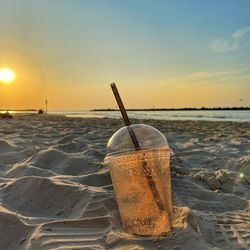 Close-up of drink on beach against sunset