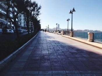 Empty footpath by buildings against sky