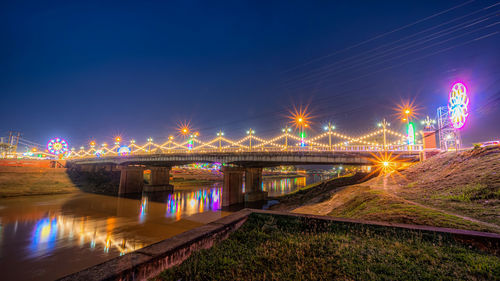 Illuminated bridge over river against sky at night