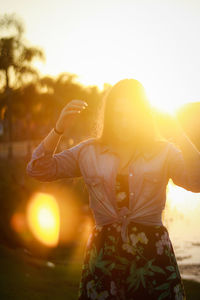 Midsection of woman standing against sun during sunset