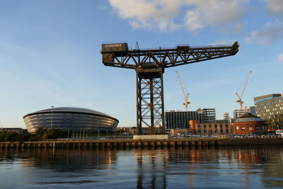 Cranes by river against sky in city