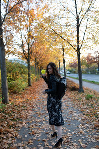 Portrait of woman holding flower while standing by trees during autumn