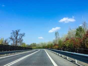 Empty road by trees against blue sky