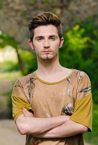Portrait of handsome young man with arms crossed standing at park