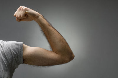 Midsection of man with arms raised against gray background