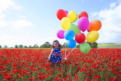 Girl holding colorful balloons while standing on field against sky