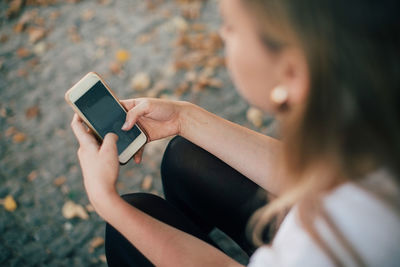 High angle view of young woman using mobile phone while sitting on footpath