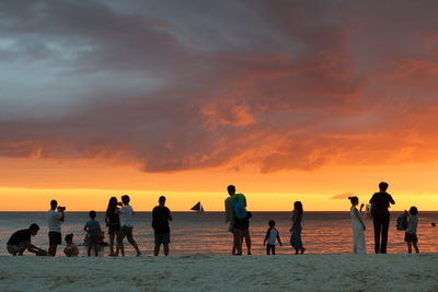 People on beach against sky during sunset