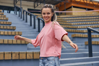 Portrait of smiling young woman standing against railing