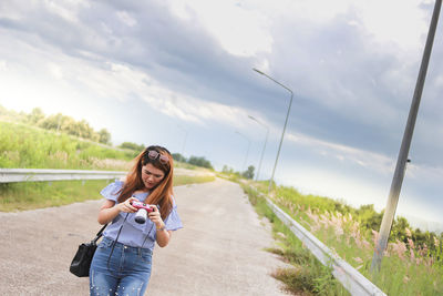 Portrait of smiling woman standing on road against sky