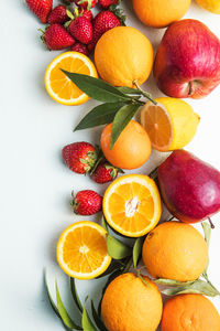 Flat lay of citrus fruits like lime, orange and lemon with leaves on light colored background.