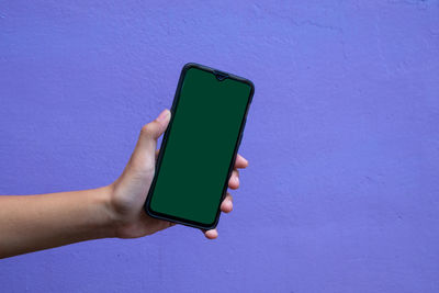 Close-up of hand holding mobile phone against wall