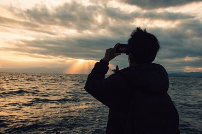 Man photographing sea against sky during sunset