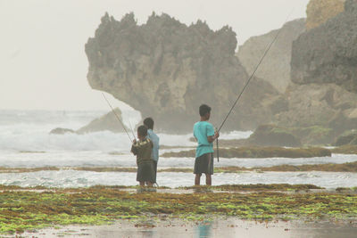 Boys fishing in sea against sky