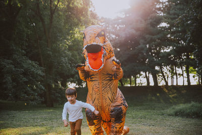 Person wearing dinosaur costume chasing boy in park