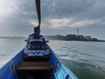 Rear view of boat in sea against cloudy sky