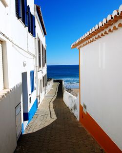 Footpath amidst buildings by sea against sky