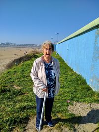 Full length portrait of senior woman with walking cane standing on land during sunny day