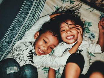 Directly above shot of happy girl lying down with brother on bed at home