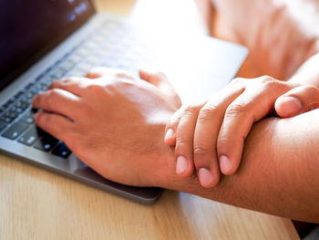 Cropped hand holding hand while using laptop at office