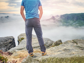 Handsome man with hands in his pockets, looking away standing near cliff edge. red baseball cap 