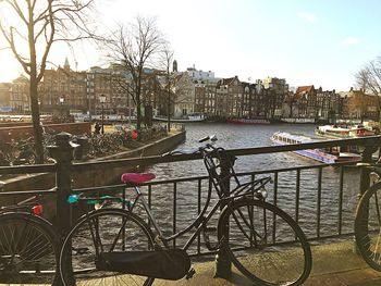 Bicycle by canal in city against sky