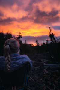 Rear view of woman sitting on field against sky during sunset