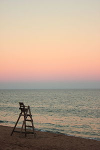 Chair on beach against sky during sunset