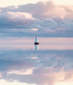 Lighthouse in sea against sky during sunset