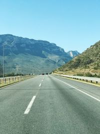 Road leading towards mountains against clear sky