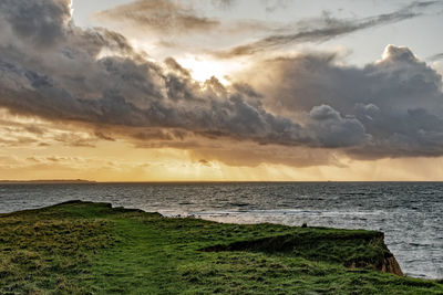 Scenic view of sea against dramatic sky during sunset