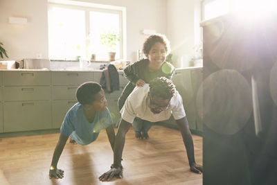 Father doing push-ups while carrying son on back in kitchen at home