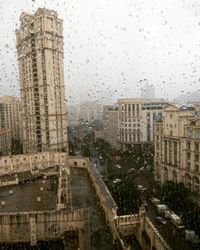 City against sky seen through wet window during rainy season