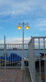 Illuminated street light by sea against sky