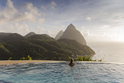 Scenic view of infinity pool with woman relaxing against sky