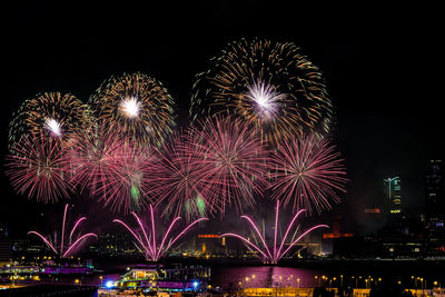 Firework display over illuminated cityscape against sky at night