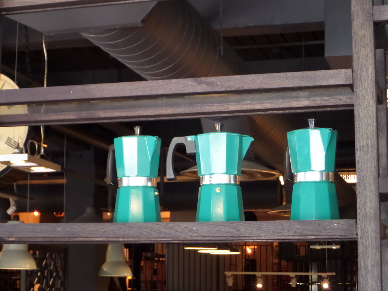 Three blue coffee pots in a row on a shelf.