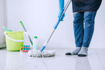 Low section of person cleaning floor with mop against wall at home